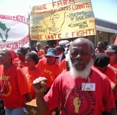 A group of people on a protest wearing red tshirts with fists raised. Banner says Organise, Unite and Fight