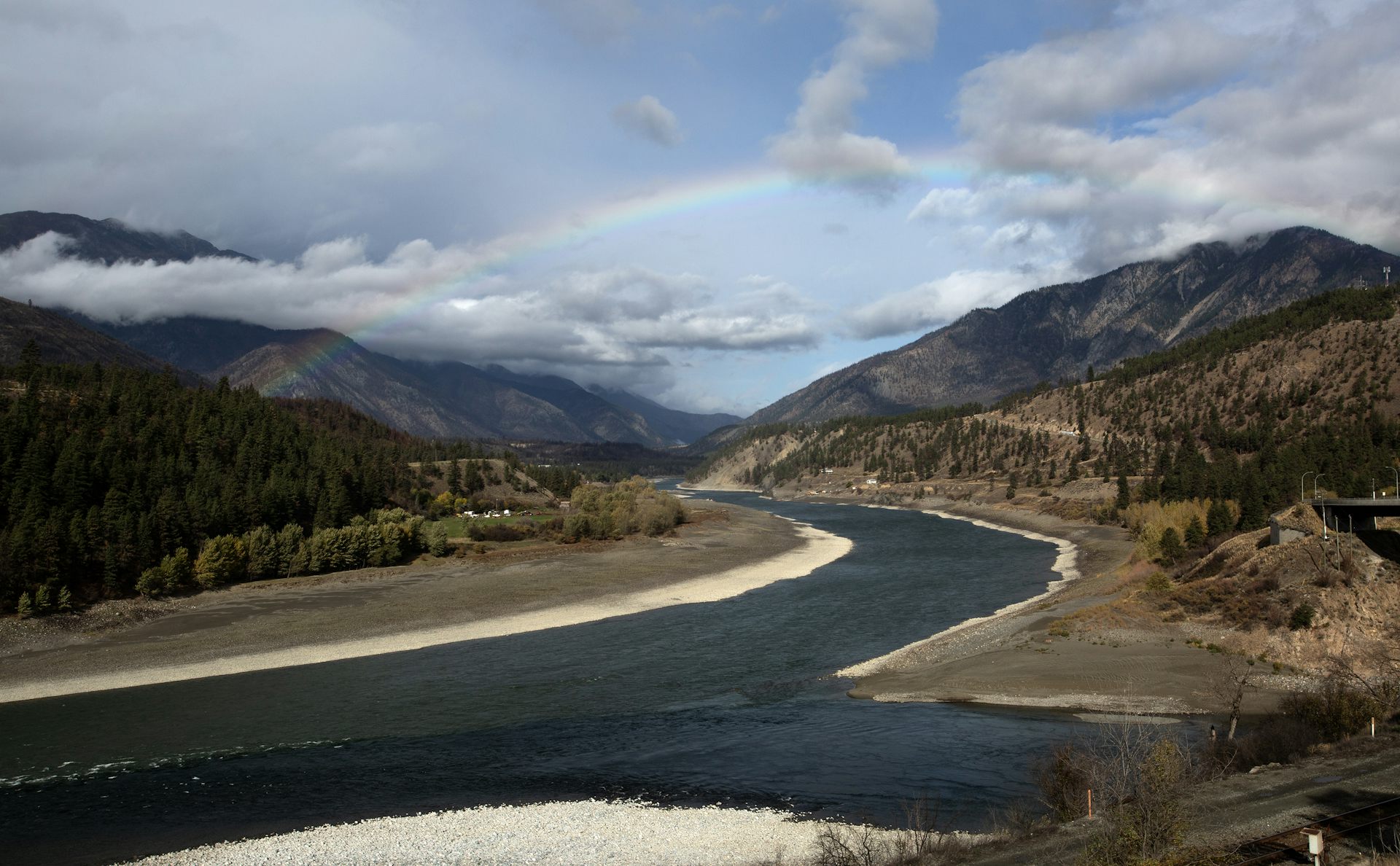 A rainbow over a river with mountains on either side.