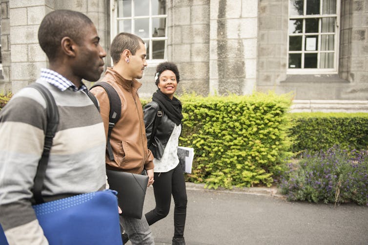 Three college students -- two young men and a young woman -- walk on campus.