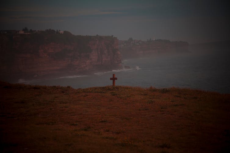 A cross sits at the edge of the shore, looking out onto the ocean.