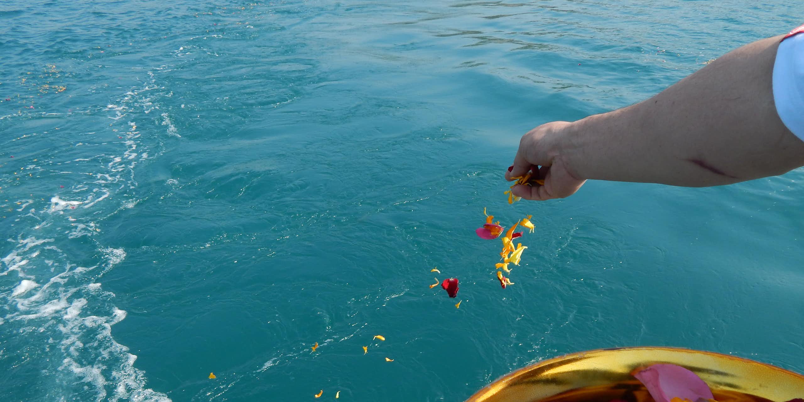 A person scatters flowers over the ocean.
