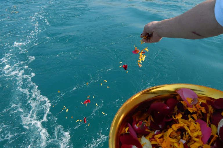 A person scatters flowers over the ocean.