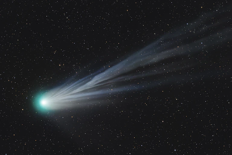 A bright green globe with a wispy tail against a black night sky.