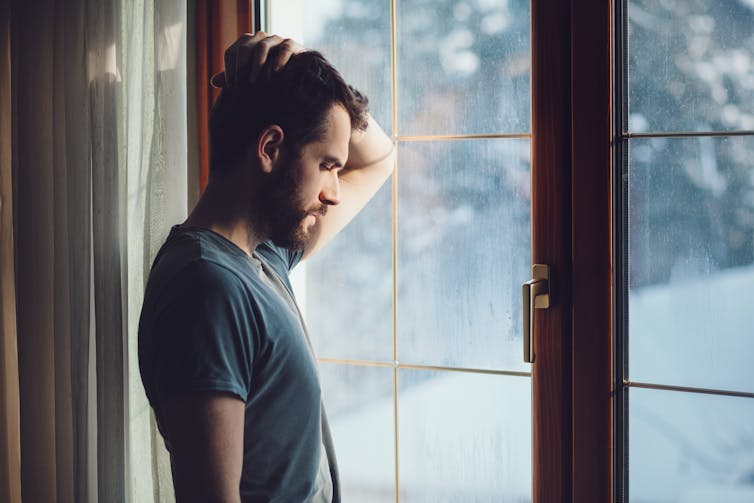 A young man looking out the window, appears depondent.