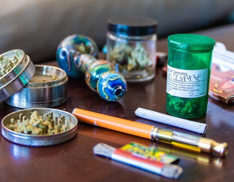 Marijuana buds and THC oil with various smoking accessories lying on a table.