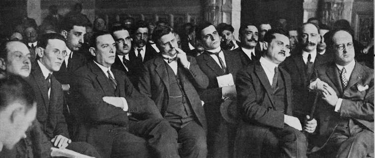 Diputados trajeados sentados escuchando un discurso