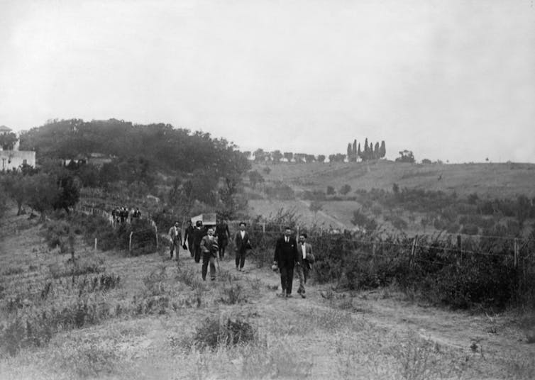 A line of people follow a coffin being carried through the Italian countryside.