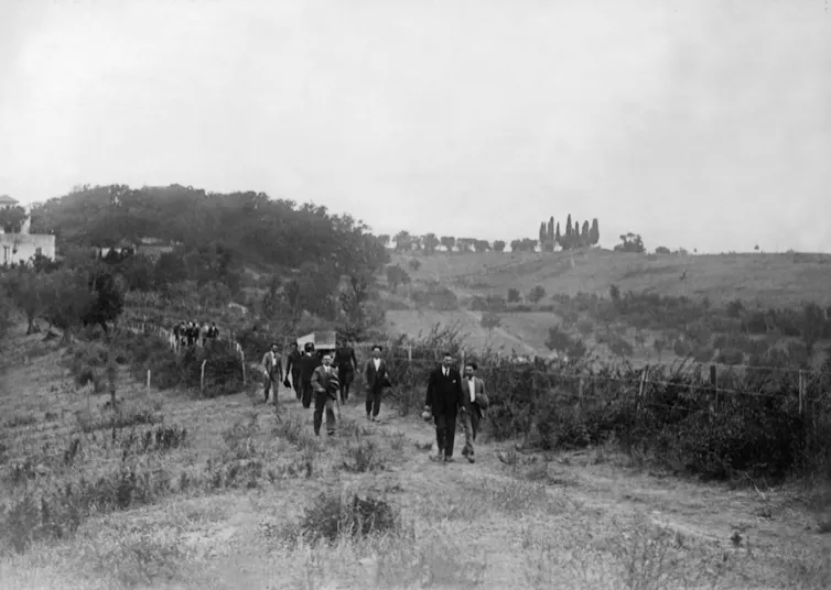 A line of people follow a coffin being carried through the Italian countryside.