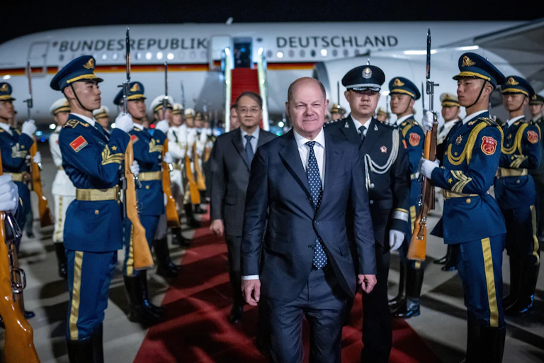 Germany's chancellor, Olaf Scholz, exits a plane and walks between Chinese soldiers.