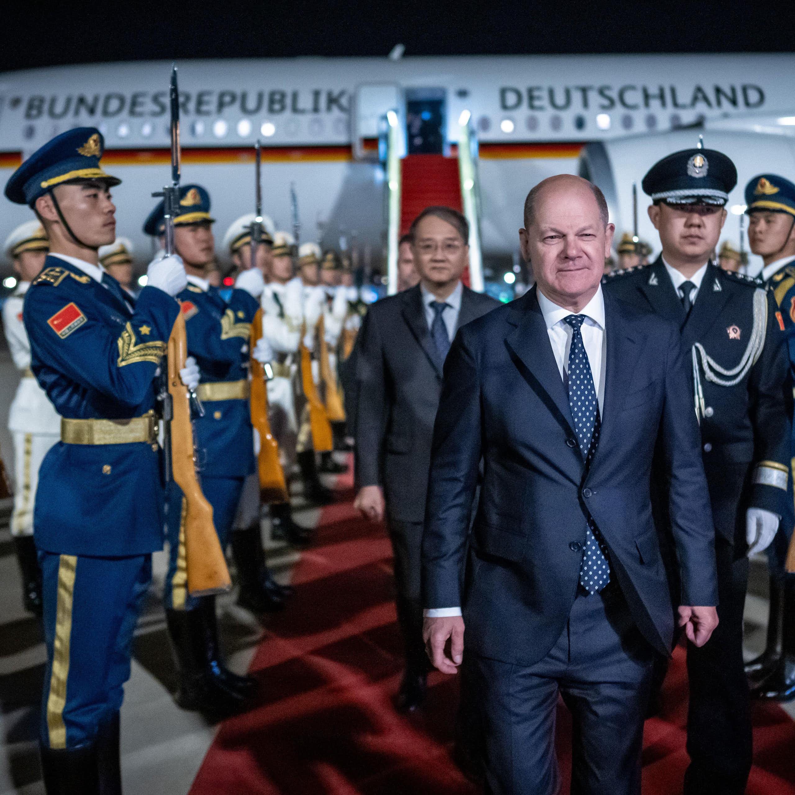 Germany's  chancellor, Olaf Scholz, exits a plane and walks between Chinese soldiers.