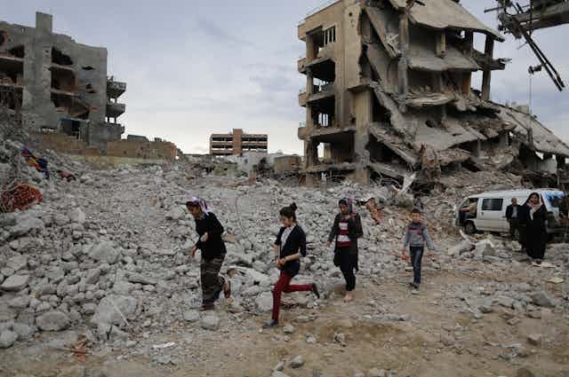 Four children walking over rubble in a war-damaged town.