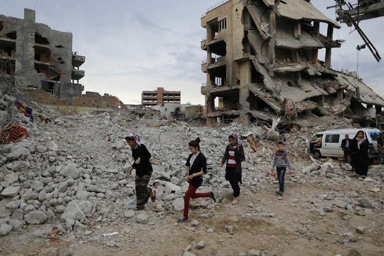Four children walking over rubble in a war-damaged town.