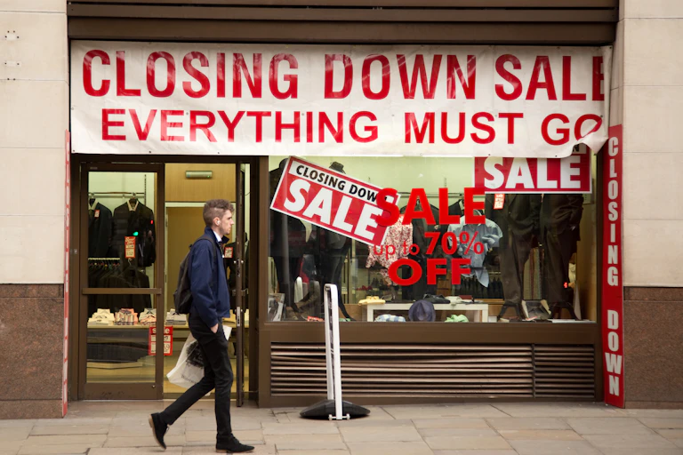 Man walking past a shop with a closing down sale sign in the window