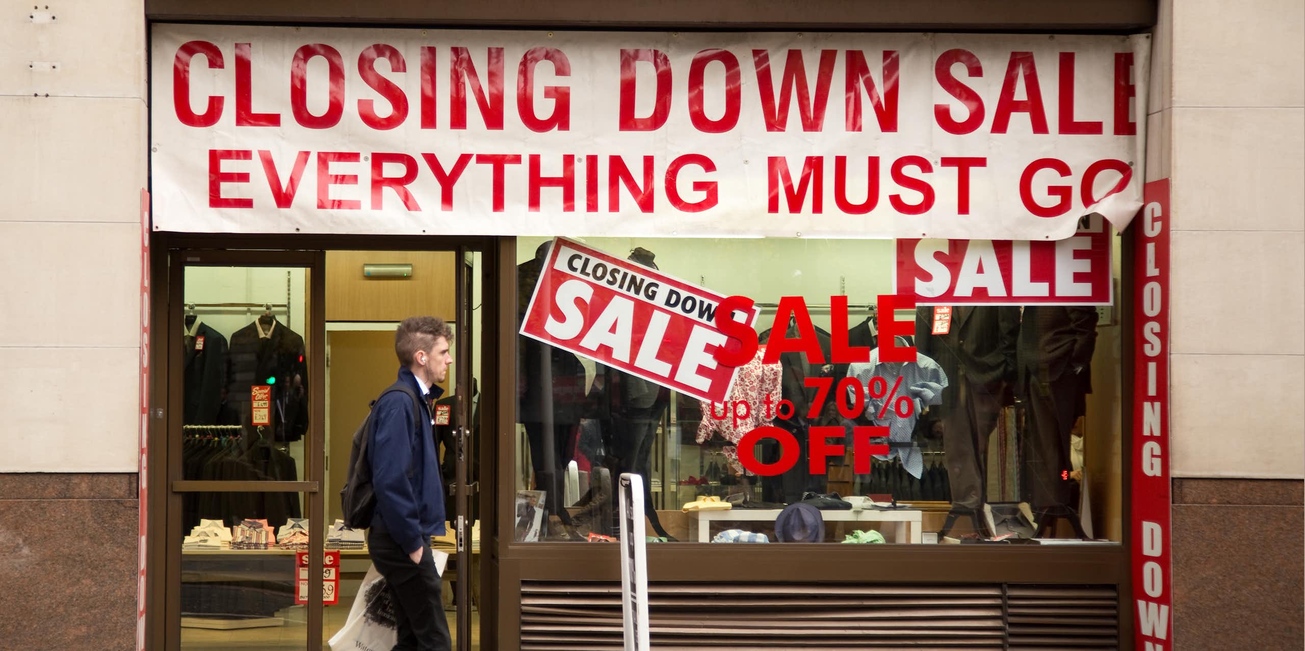 Man walking past a shop with a closing down sale sign in the window