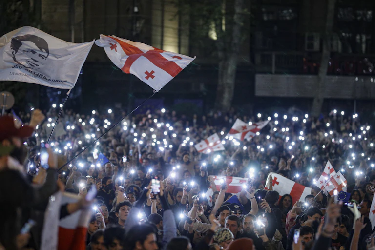 A crowd of protestors holding Georgian flags and their phones with the light switched on.