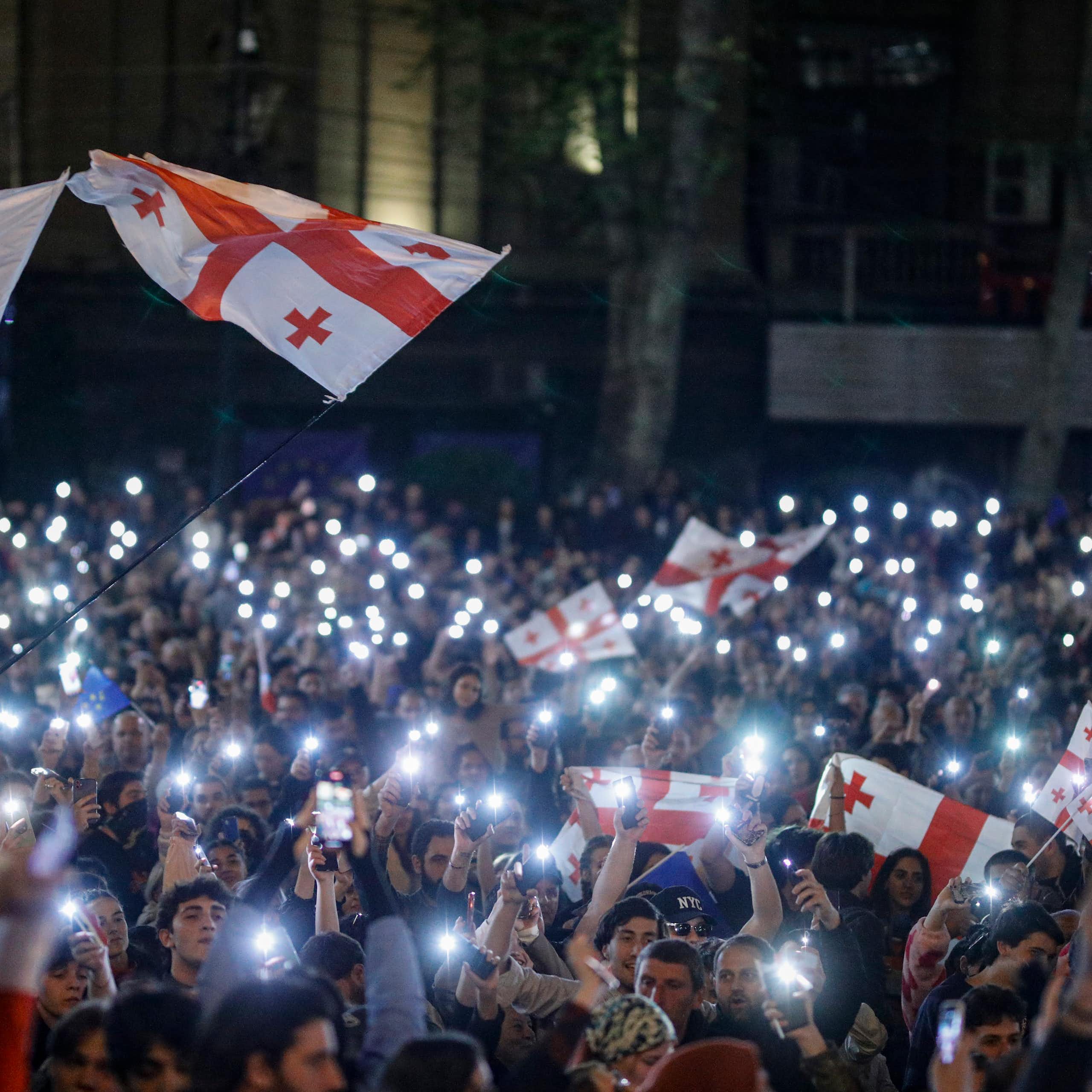 A crowd of protestors holding Georgian flags and their phones with the light switched on.