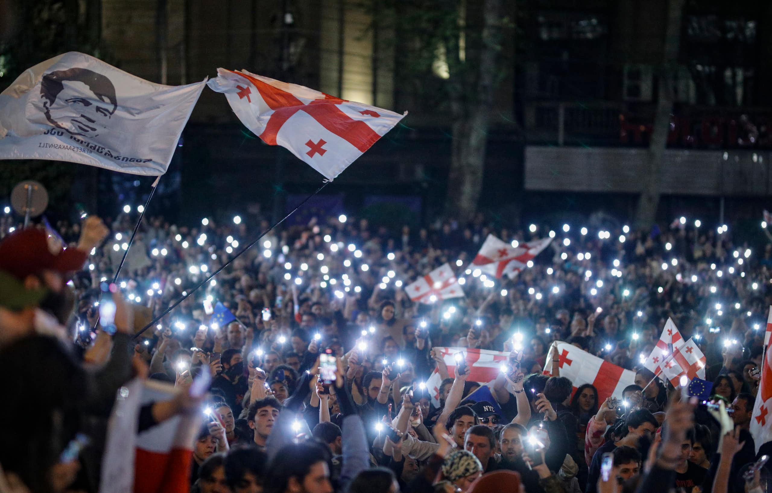 A crowd of protestors holding Georgian flags and their phones with the light switched on.