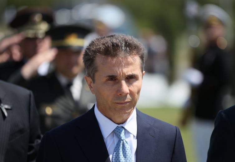 A man dressed in suit in front of armed forces members.