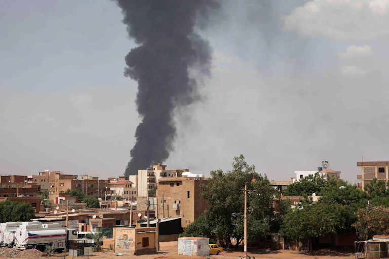 A thick plume of smoke rising in a column above a city.