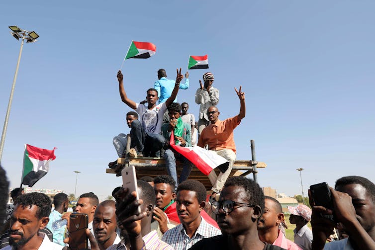 A crowd of people holding Sudan flags on a sunny day.