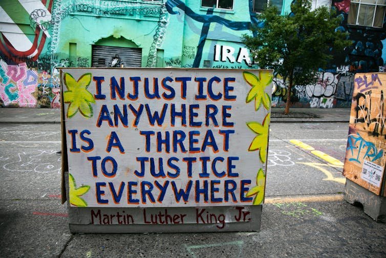 A sign is painted with large words that describe the meaning of the word injustice.