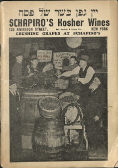 A yellowed advertisement for Schapiro's Kosher Wines featuring a black and white photo of men pouring grapes into a barrel.
