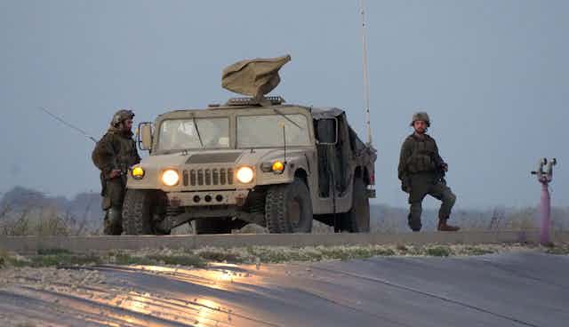 Two Israeli soldiers and an armoured car on patrol in the Gaza Strip.