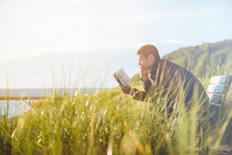 A man reading on a bench by the sea