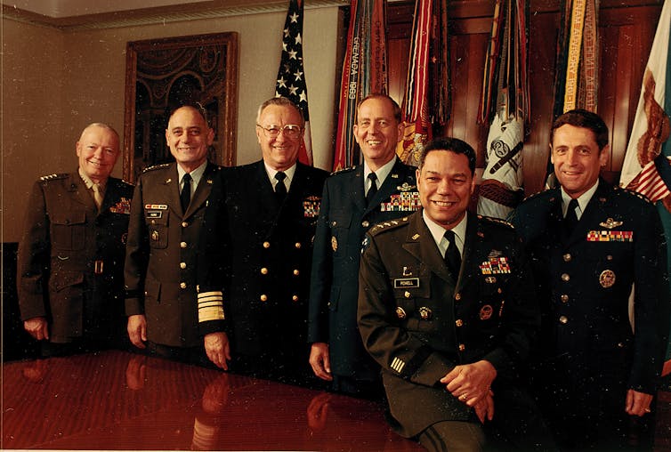 A group of men stand around the table while wearing military uniform