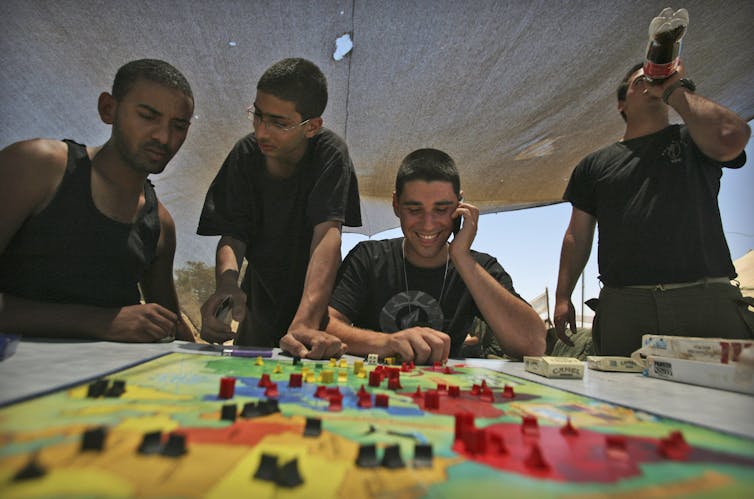 Soldiers smile as they play a board game that has plastic pieces on a colourful world map.