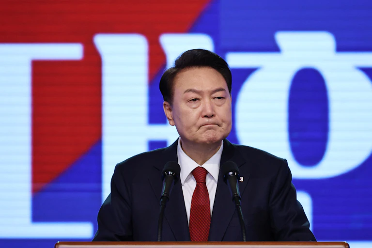 A man dressed in a suit and red tie frowns.