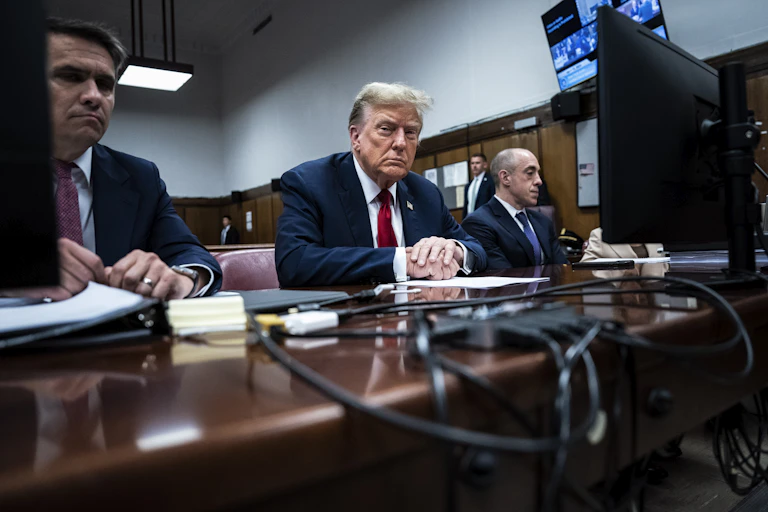 People sit at a desk with papers and computer cables on it.