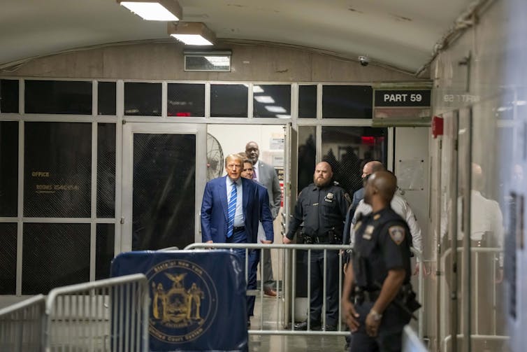 A man walks out a door that is guarded by a police officer.