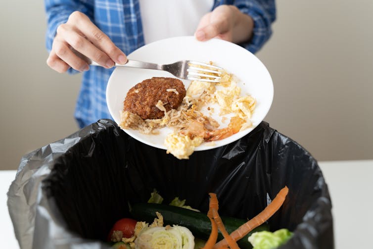 A person pours wasted food into a garbage can.