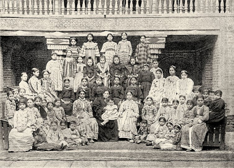 A black and white photo of several rows of girls in long dresses, posing for a formal photograph.