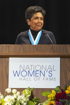 A middle-aged South Asian women speaks from behind a podium