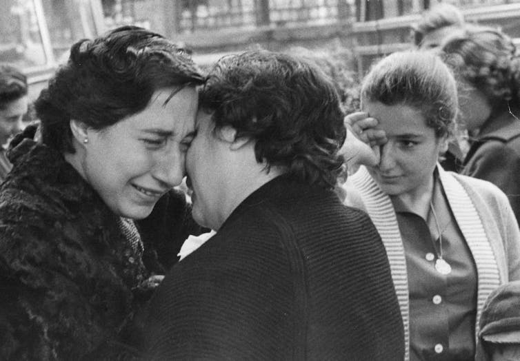 A black and white photo of three women crying as they embrace.