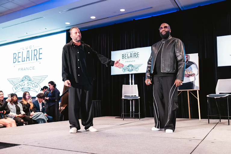 Two men stand on a stage wearing black leisurewear.