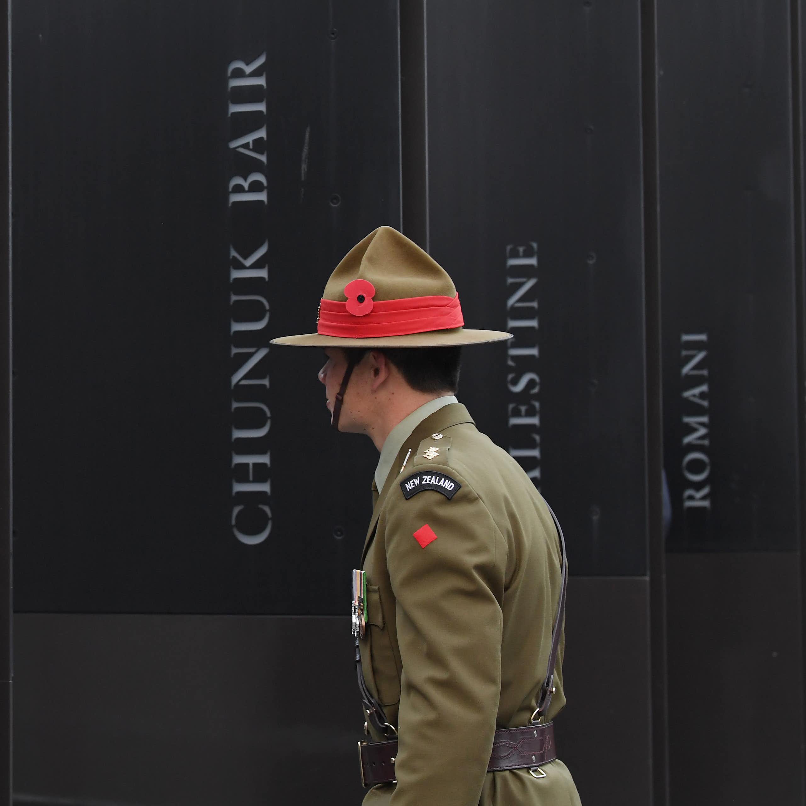 New Zealand soldier in front of World War 1 memorial showing battle names