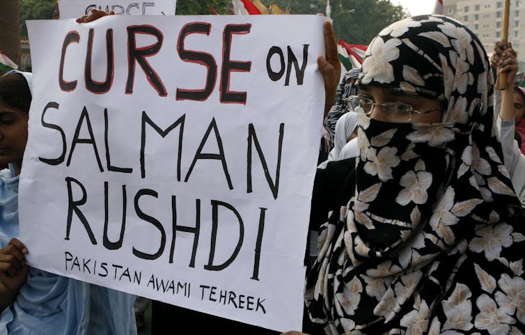 protesters hold a sign: CURSE ON SALMAN RUSHDI
