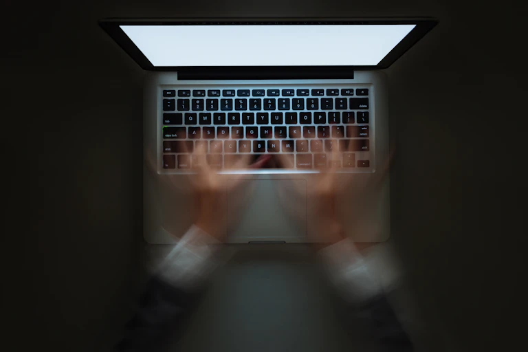 View from above of a woman's hands typing very fast in a blur on a laptop