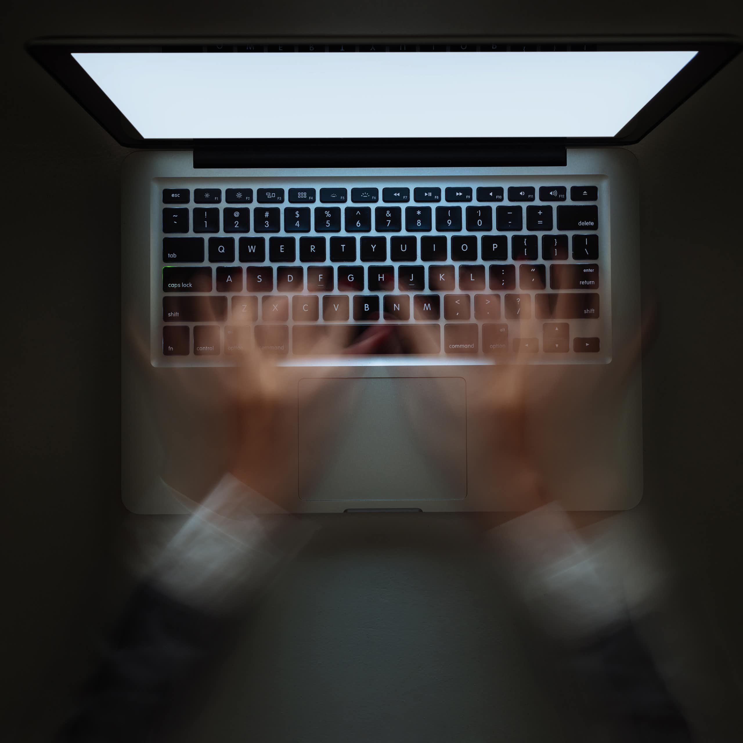 View from above of a woman's hands typing very fast in a blur on a laptop