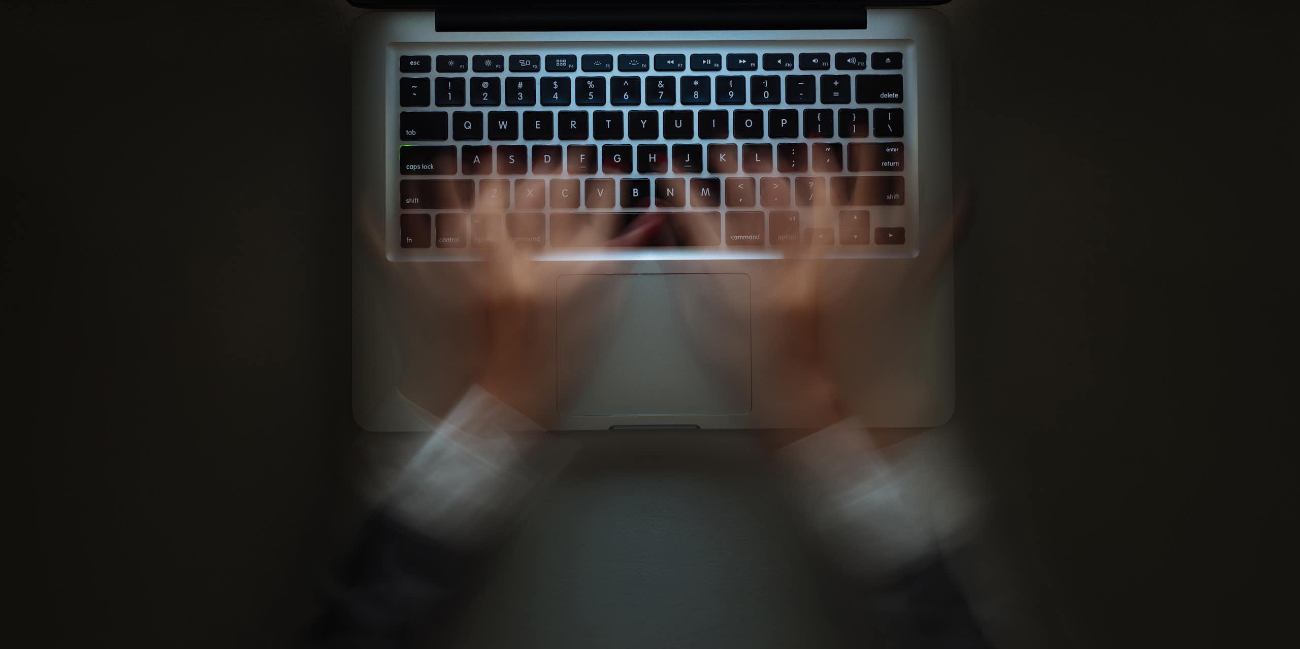 View from above of a woman's hands typing very fast in a blur on a laptop
