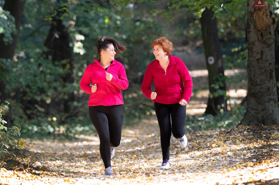 Two middle-aged women run in a forest.
