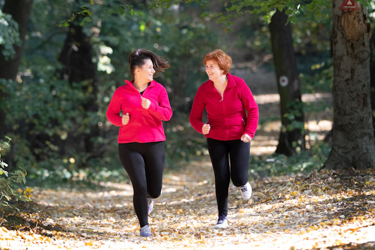 Two middle-aged women run in a forest.