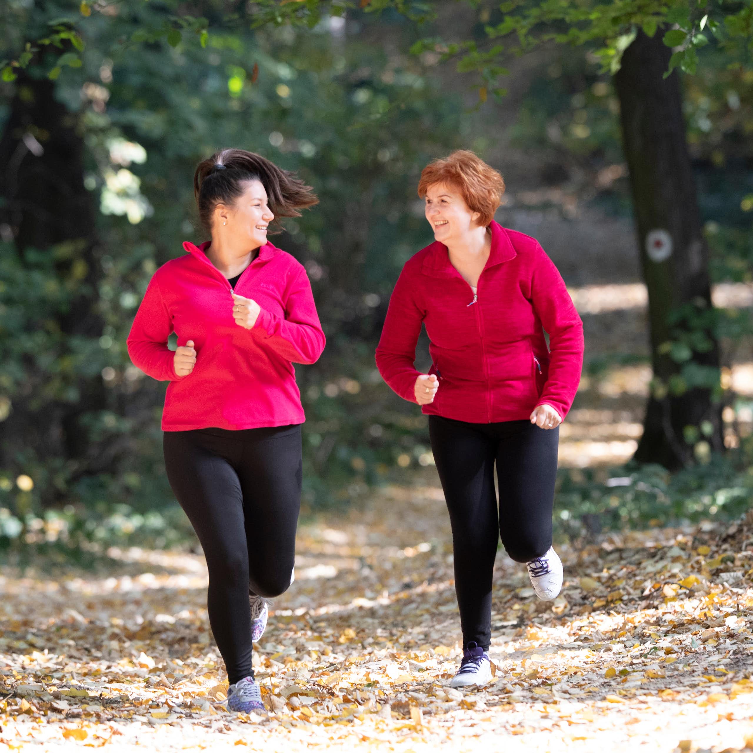 Two middle-aged women run in a forest.