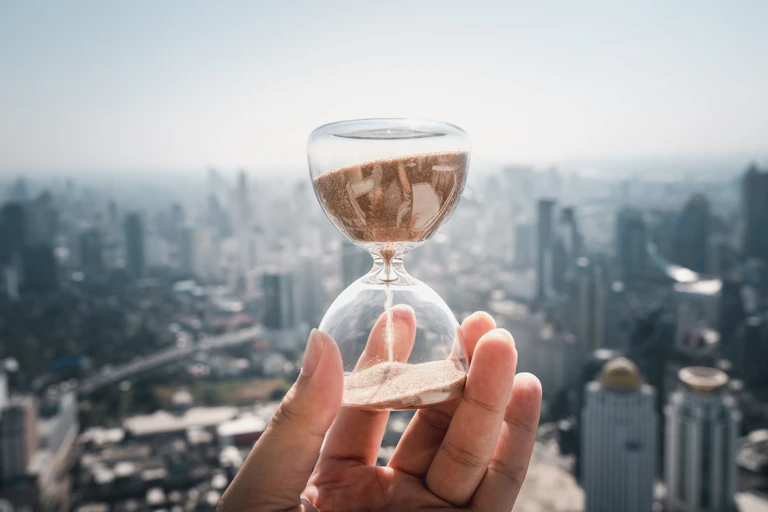 Una mano sujeta un reloj de arena ante un paisaje urbano.