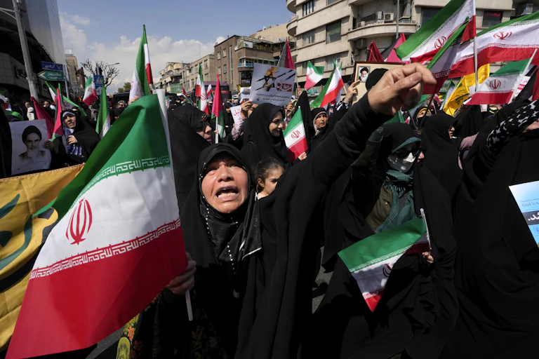 A woman in a black hijab shouts while holding a green, white and red flag.