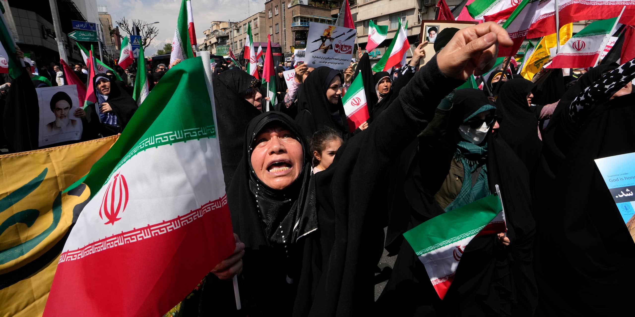 A woman in a black hijab shouts while holding a green, white and red flag.