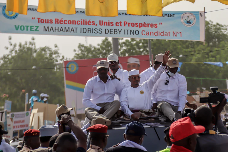 Man wearing white kaftan dress and cap surrounded by other men wearing white shirts.